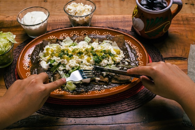Persona che mangia Enfrijoladas servita in un piatto di argilla Cibo messicano Tacos di fagioli con panna e formaggio