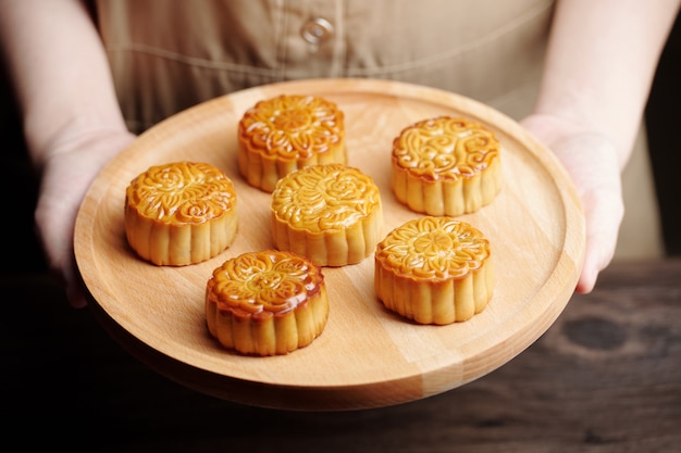 Persona che offre vassoio di legno con bellissime torte lunari preparate per il festival di metà autunno