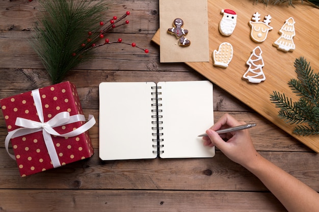 Persona che scrive sul taccuino aperto con confezione regalo e gustosi biscotti fatti in casa di Natale