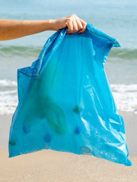 Persona che tiene il sacchetto della spazzatura con bottiglia di plastica riciclabile