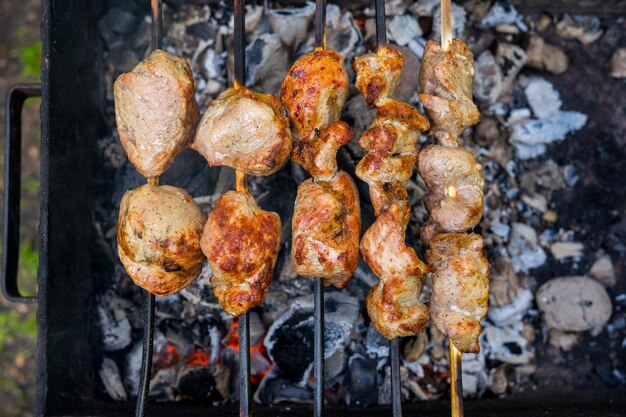 Persona che tiene un utensile e prepara la carne alla griglia nel cortile sul retro in una giornata di sole. Foto di alta qualità