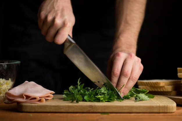 Persona che trita le mani e il coltello visibili del cuoco unico del prezzemolo fresco