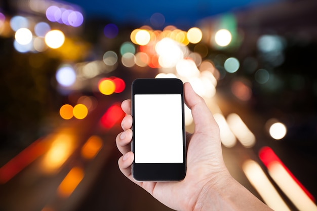 Persona che utilizza smartphone porta schermo bianco a portata di mano con sfondo sfocato bokeh di traffico con luce notturna.