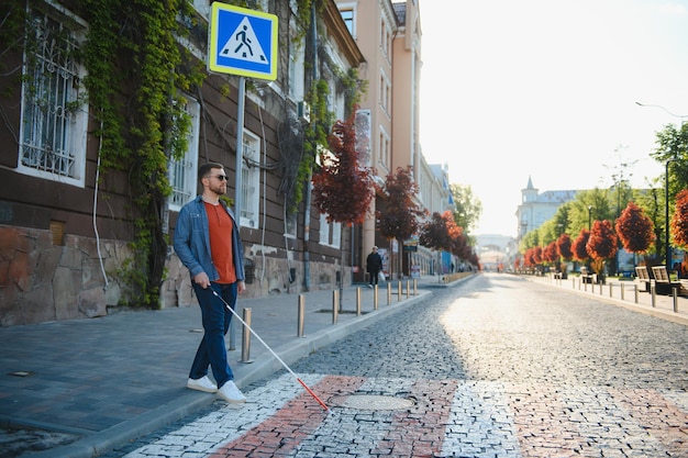 Persona cieca con il bastone bianco che attraversa la strada nel primo piano della città