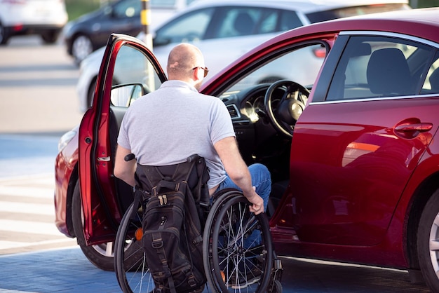 Persona con disabilità fisica che sale su un'auto rossa dalla sedia a rotelle