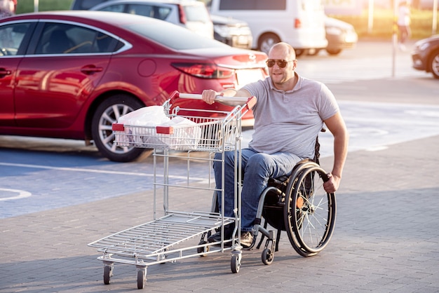 Persona con disabilità fisica che spinge il carrello davanti a sé nel parcheggio del supermercato