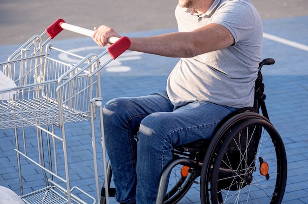 Persona con disabilità fisica che spinge il carrello davanti a sé nel parcheggio del supermercato