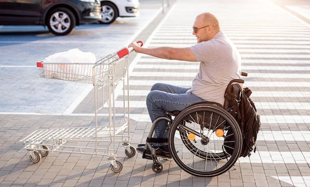 Persona con disabilità fisica che spinge il carrello davanti a sé nel parcheggio del supermercato