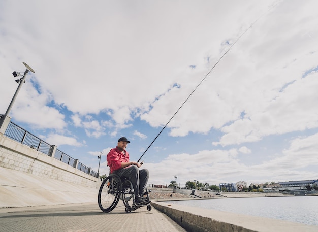 Persona con disabilità fisica che usa la pesca in sedia a rotelle dal molo dei pescatori