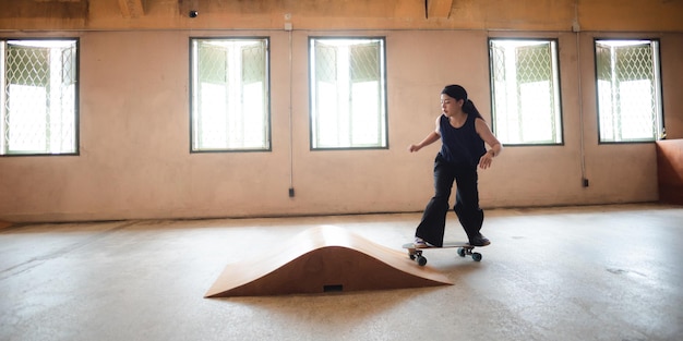 Persona della giovane donna nello stile di vita del pattino di sport ragazza teenager felice divertendosi con lo skateboard nell'attività urbana di moda dei pantaloni a vita bassa della palestra di sport alla moda