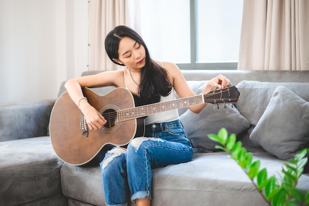 Persona di donna che suona uno strumento musicale per chitarra acustica a casa giovane stile di vita della ragazza musicista asiatica