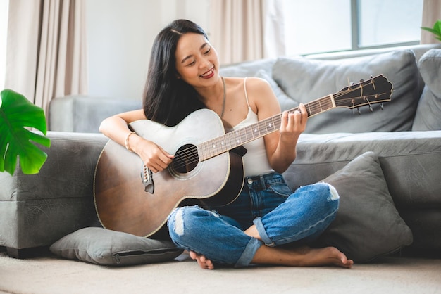 Persona di donna che suona uno strumento musicale per chitarra acustica a casa giovane stile di vita della ragazza musicista asiatica