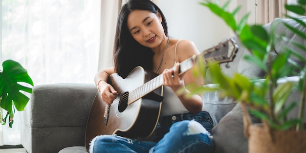 Persona di donna che suona uno strumento musicale per chitarra acustica a casa giovane stile di vita della ragazza musicista asiatica