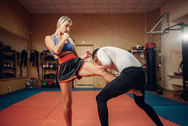 Persona di sesso femminile fa un calcio all'inguine, allenamento di autodifesa con personal trainer maschile, interno della palestra. Donna in formazione, pratica di autodifesa