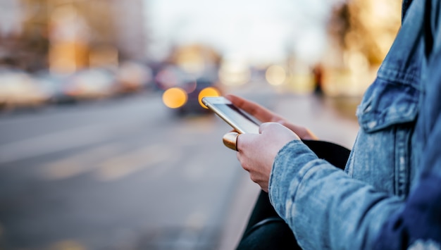 Persona di sesso femminile in giacca di jeans utilizzando il telefono in via della città. Avvicinamento.