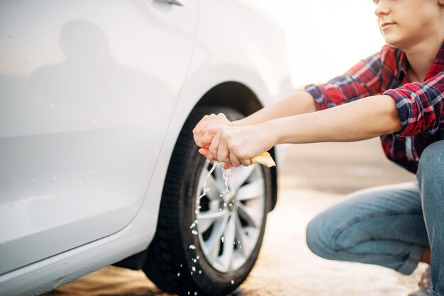 Persona di sesso femminile su autolavaggio self-service, processo di autolavaggio. Lavaggio del veicolo all'aperto in una giornata estiva. La donna stringe la spugna dopo la pulizia dell'automobile