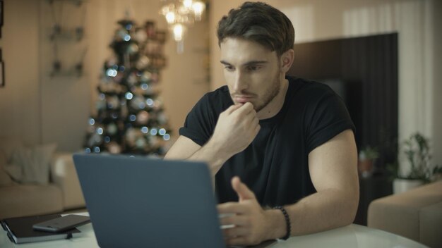 Persona di sesso maschile che utilizza il computer portatile in casa durante le vacanze di Natale Uomo che lavora al computer