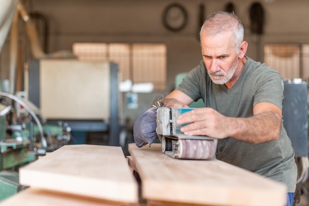 Persona di sesso maschile concentrata sul lavoro con una levigatrice manuale che lucida una tavola di legno