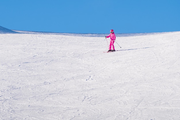 Persona felice in giacca rossa che scia in discesa sotto il sole splendente su cielo blu con alte montagne innevate sullo sfondo Movimento sfocato