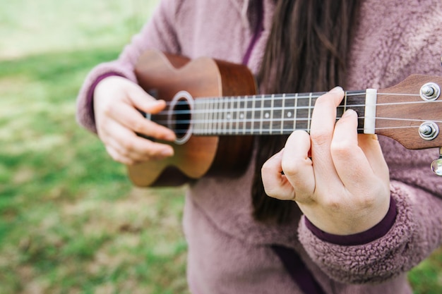 Persona femminile irriconoscibile che gioca ukelele in piedi sull'erba.