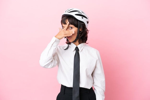 Persona giovane ragazza con un casco da bici isolato su sfondo rosa che copre gli occhi con le mani e sorride