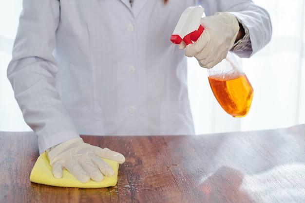 Persona in camice da laboratorio superficie di pulizia del tavolo in legno con spray disinfettante per uccidere batteri e virus