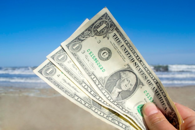 Persona in possesso di tre banconote da un dollaro di carta sullo sfondo delle onde del mare e del mare