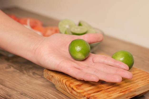 Persona in possesso di un limone verde con un coltello sul tavolo di legno nella sua cucina