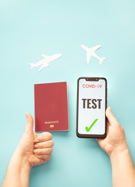 persona in possesso di uno smartphone che mostra un test covid e un passaporto su uno sfondo blu concetto di viaggio