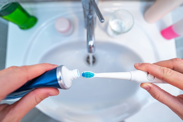 Persona lavarsi i denti con spazzolino ad ultrasuoni e utilizzando prodotti dentali per lavarsi i denti e per l'alito fresco nel bagno di casa