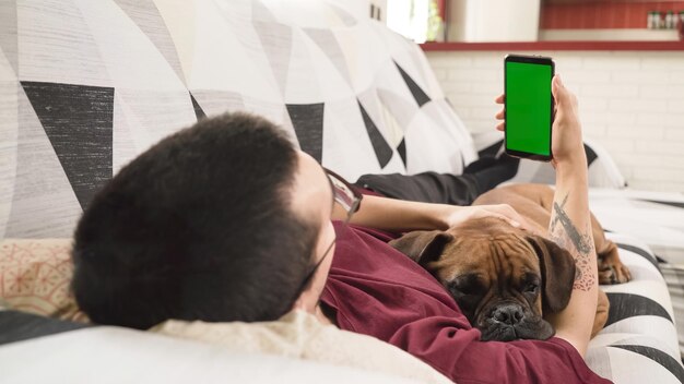 Persona sdraiata su un divano con il suo cane mentre tiene in mano un telefono cellulare con uno schermo verde