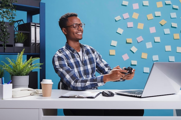 Persona sorridente felice dell'ufficio con il controller di gioco moderno che gioca ai videogiochi divertendosi al lavoro. Allegro giocatore adulto con gamepad elettronico che si diverte con attività ricreative per il tempo libero.