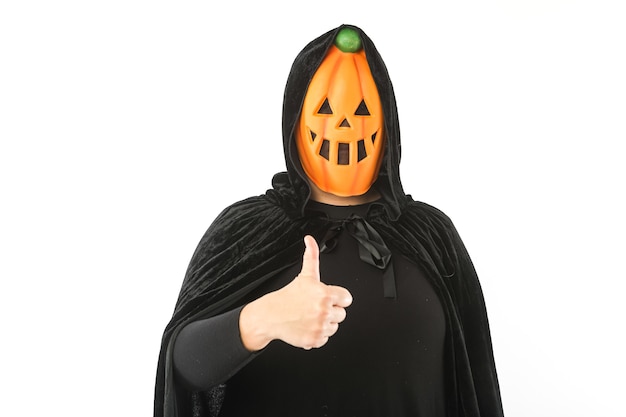 Persona vestita con maschera di zucca Jack-o.-lantern e mantello di velluto con cappuccio, alzando il pollice, su sfondo bianco. Carnevale, Halloween e il concetto di giorno dei morti.