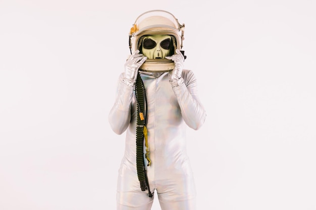 Persona vestita con un abito d'argento e una maschera aliena verde, che indossa un casco da cosmonauta, su sfondo bianco
