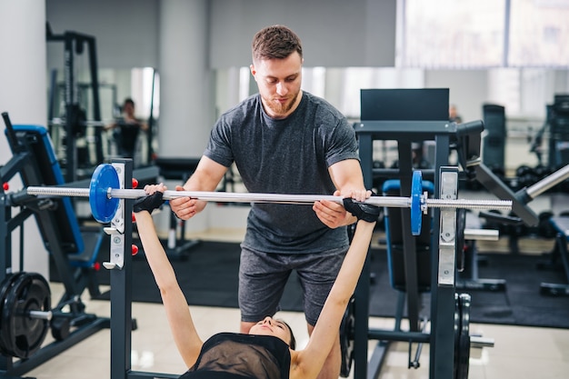 Personal trainer che aiuta una giovane donna a sollevare un bilanciere mentre si allena in palestra, messa a fuoco selettiva.