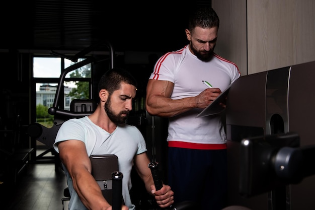 Personal Trainer che mostra al giovane come allenarsi indietro sulla macchina in palestra