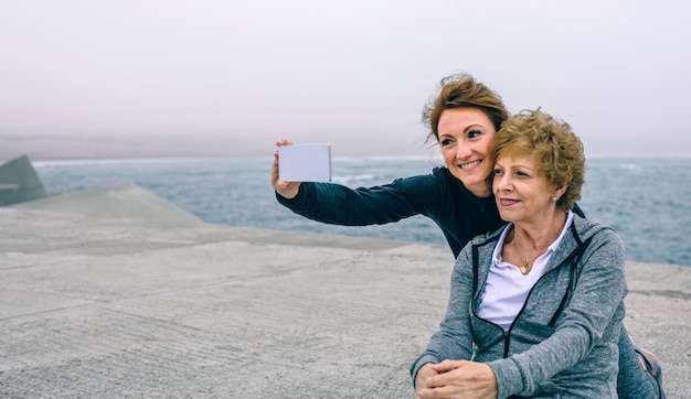 Personal trainer che prende selfie con una donna anziana dal molo del mare