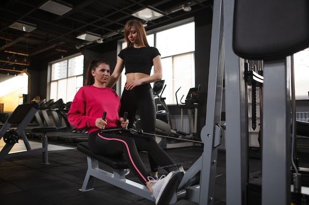 Personal trainer e il suo cliente utilizzando una macchina da palestra per fila di cavi seduti