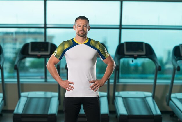 Personal Trainer in piedi forte in palestra Centar Fitness sfondo con Copyspace e flettendo i muscoli Muscoloso uomo atletico in posa