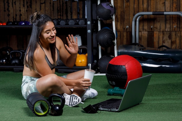 Personal trainer saluta il computer dopo aver tenuto una lezione online bevendo un drink