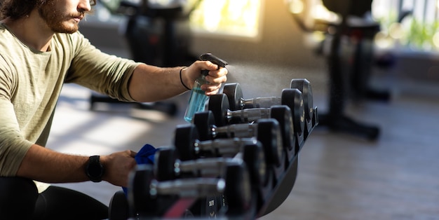 Personale di fitness pulizia macchine per esercizi con spray disinfettante alcolico in palestra