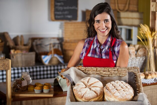 Personale femminile sorridente che tiene cesto di vimini di pane al bancone