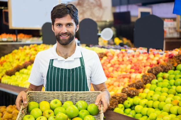 Personale maschile sorridente che tiene un canestro della mela verde al supermercato