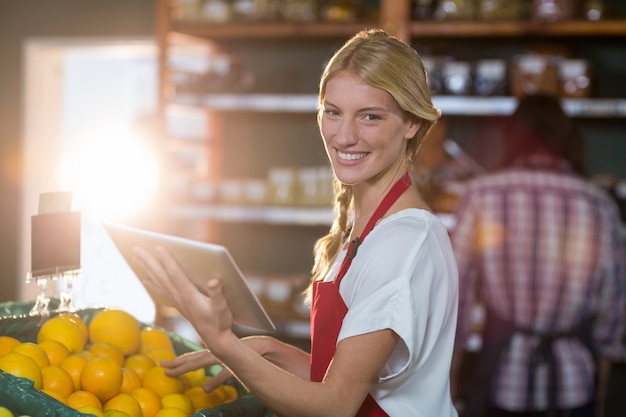 Personale sorridente che utilizza compressa digitale mentre controllando frutti nella sezione organica