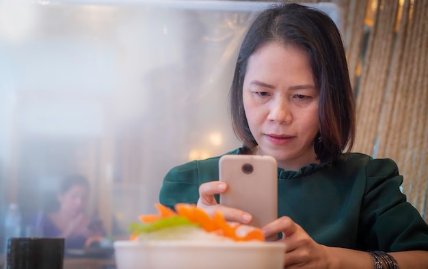 Personalità di una donna asiatica in un ristorante giapponese che utilizza uno smartphone per scattare foto di cibo