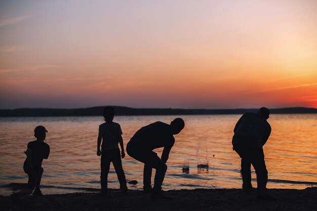 Persone al tramonto che lanciano pietre nell'acqua