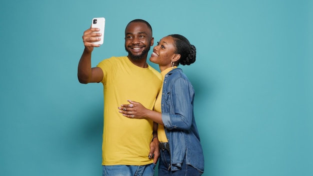 Persone allegre che usano il cellulare per fare selfie insieme in studio. Uomo e donna che scattano foto con lo smartphone e si divertono davanti alla telecamera. Coppia spensierata sentirsi felice.