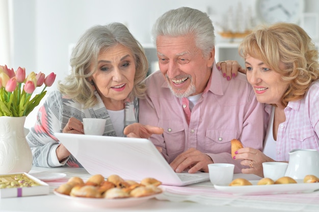 Persone anziane felici con il computer portatile che beve il tè in cucina