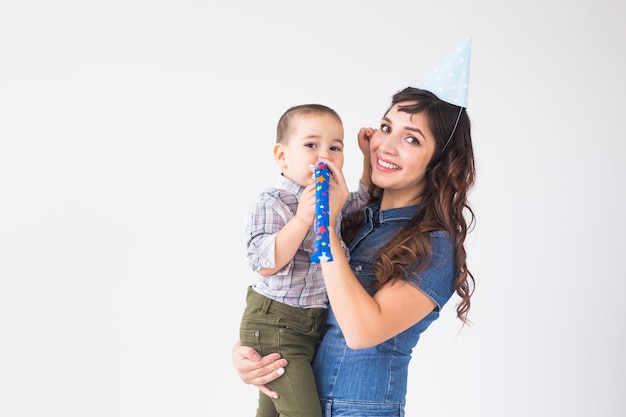 Persone, bambini e concetto di vacanza - Affascinante madre tiene il figlio che indossa il cappello di compleanno sopra il muro bianco con lo spazio della copia.