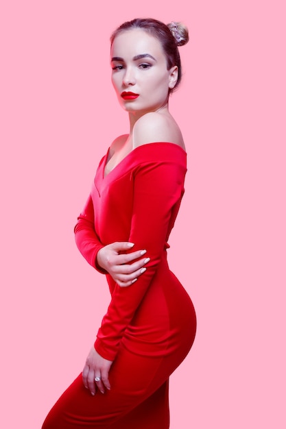 Persone, bellezza, moda, stile di vita e concetto di colore - ritratto in studio di moda di splendida donna sensuale con i capelli scuri indossa un elegante abito rosso su sfondo rosa